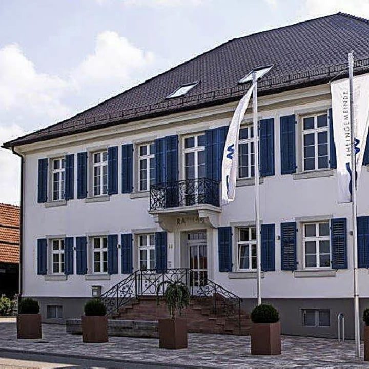 Rathaus mit blauen Fensterläden und Fahnen, Standort für Unsere Grüne Glasfaser und lokale Dienstleistungen.