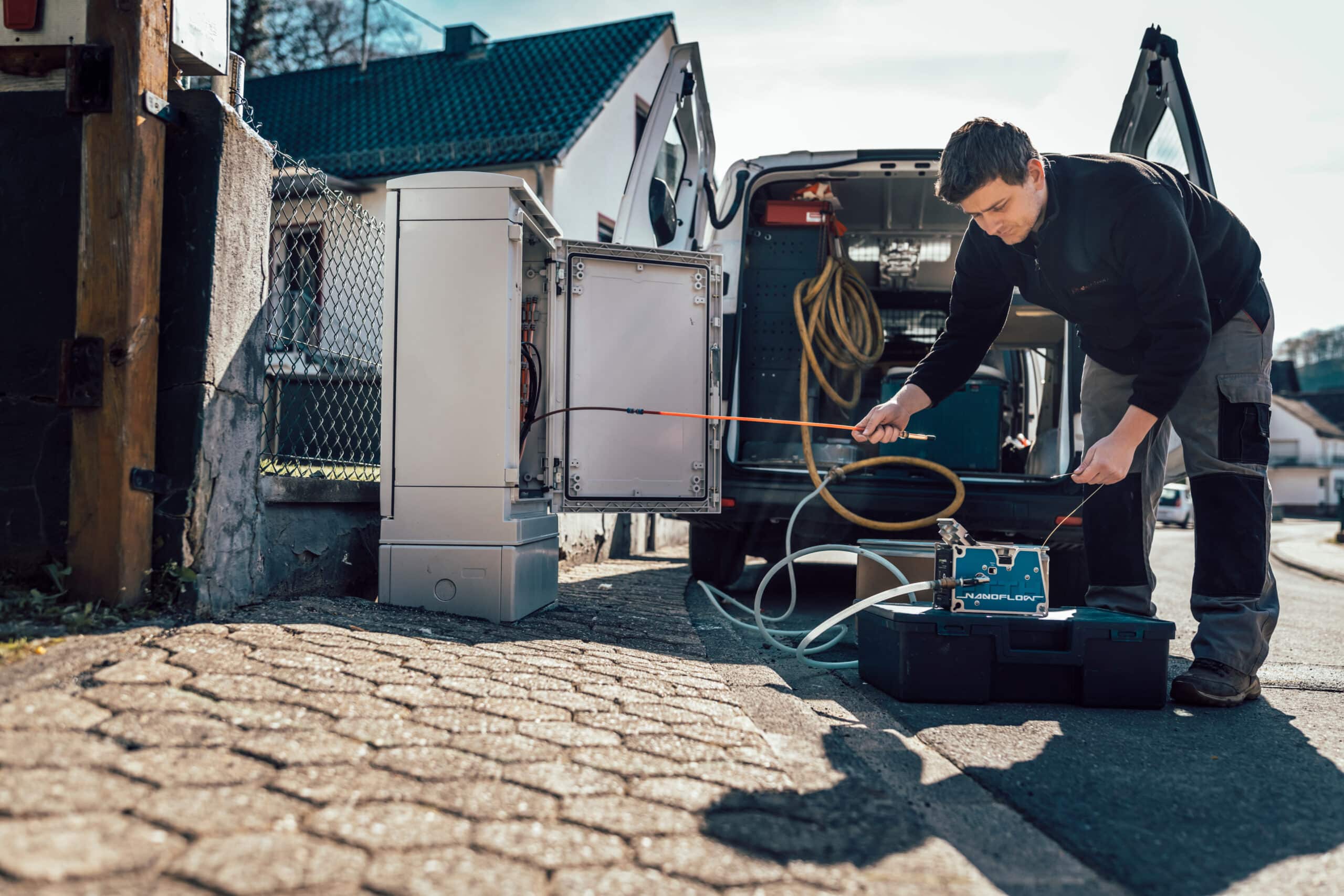 Techniker installiert Glasfaseranschluss vor einem Wohnhaus mit modernem Equipment und Fahrzeug im Hintergrund.