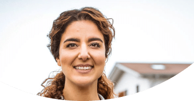 Frau mit lächelndem Gesicht vor einem Wohnhaus, symbolisiert die Vorteile von schneller Glasfaseranbindung.