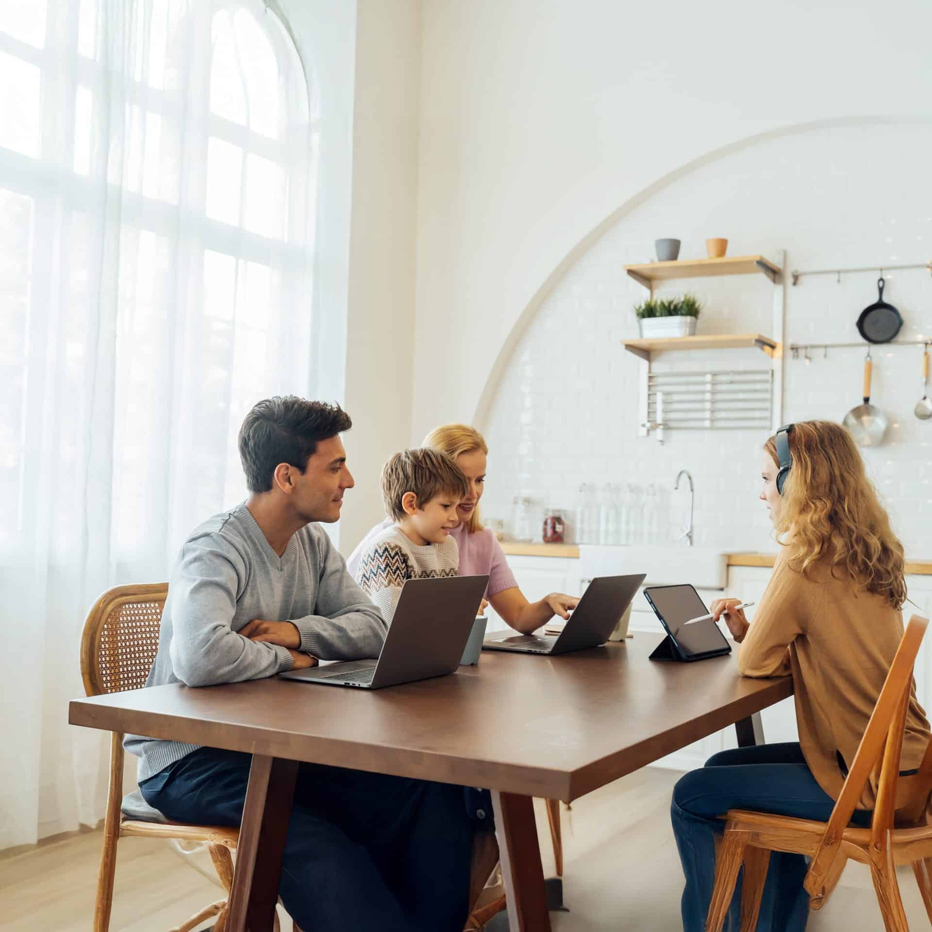 Familie nutzt moderne Technologie am Tisch, um von Zuhause aus zu lernen und zu arbeiten – Symbol für digitale Vernetzung.