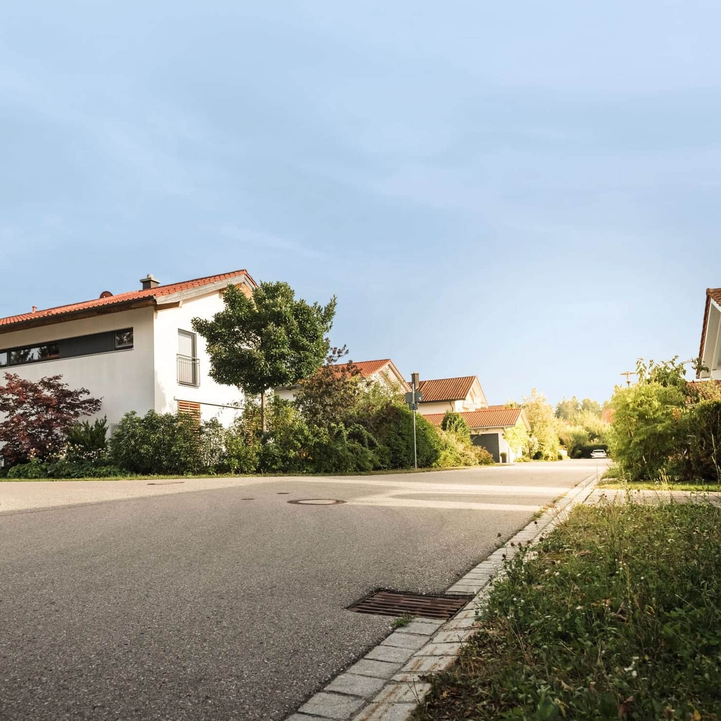 Moderne Wohnstraße mit Einfamilienhäusern und üppigem Grün, ideal für den Ausbau von Glasfaseranschlüssen.