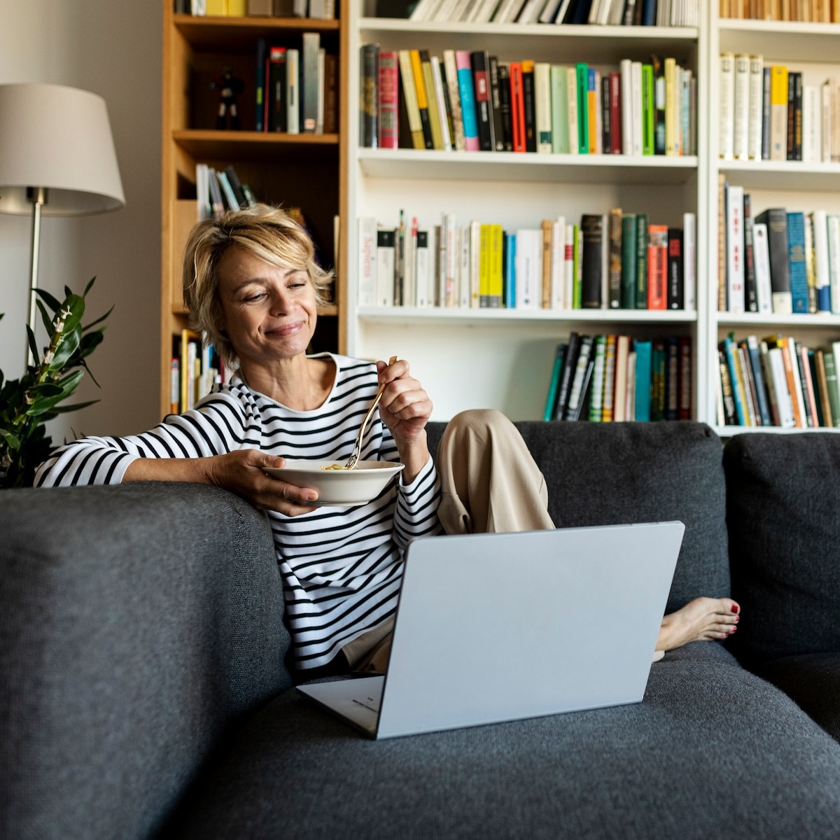 Frau genießt entspanntes Essen am Laptop auf dem Sofa, perfekt für Homeoffice mit schneller Internetverbindung von Unsere Grüne Glasfaser.